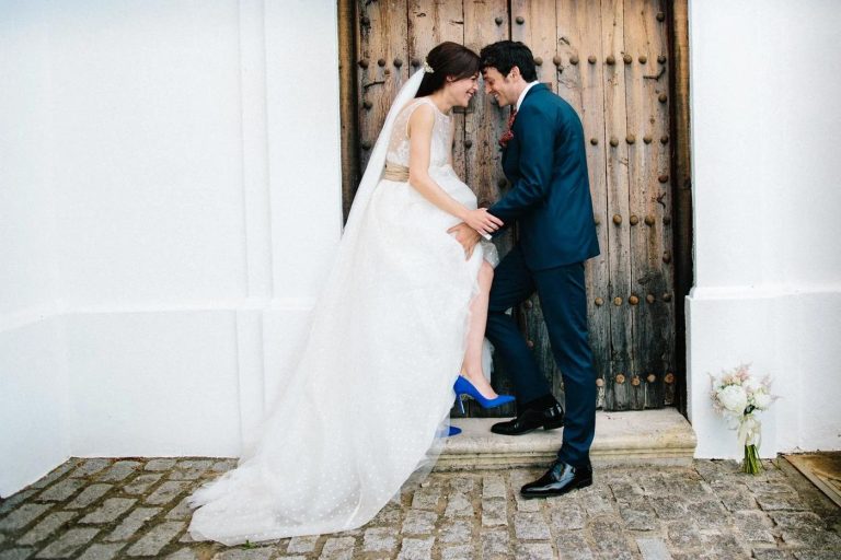 Bride and groom by a carved wooden door in a whitewashed Andalusian courtyard