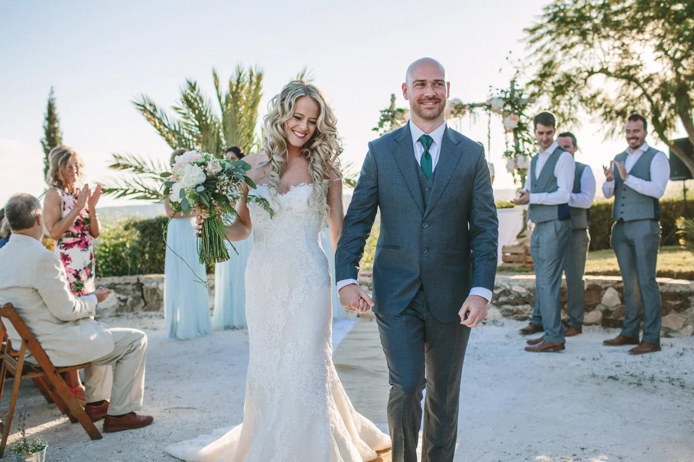 Bride and groom walking hand in hand between palm trees on their wedding day