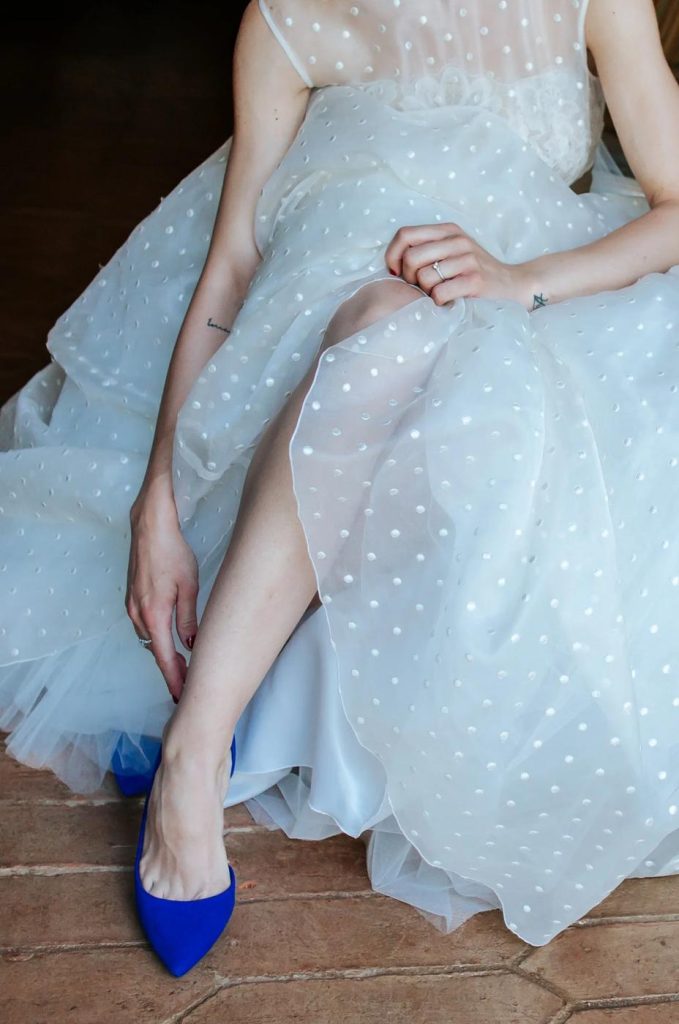 Detail of a bride slipping on blue wedding shoes beneath a polka-dot tulle gown