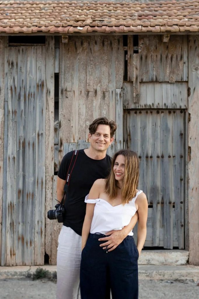 Joost and Marie, wedding photographers, standing by old wooden doors with their camera